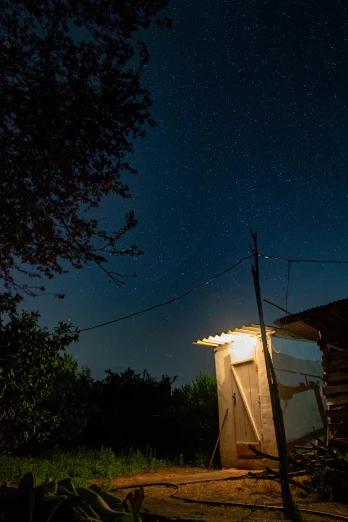 an outhouse lit up at night with the moon in the sky, by Alexander Fedosav, unsplash, light and space, ukraine. photography, late summer evening, space station light reflections, shed roof