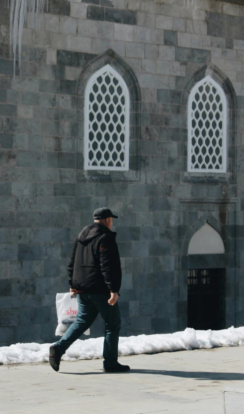 a man walking down a sidewalk in front of a building, by Ismail Acar, pexels contest winner, romanesque, ottoman sultan, bags on ground, he also wears a grey beanie, 15081959 21121991 01012000 4k