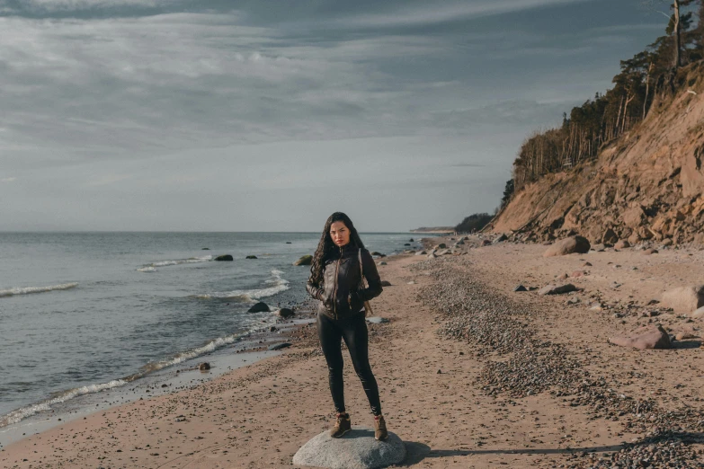 a woman standing on a rock on a beach, a portrait, by Christen Dalsgaard, pexels contest winner, avatar image, a young asian woman, fall season, greta thunberg