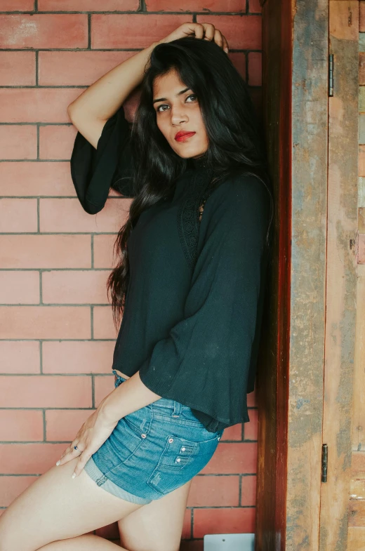 a woman standing in front of a brick wall, wearing a dark shirt and jeans, indian super model, ad image, cropped wide sleeve