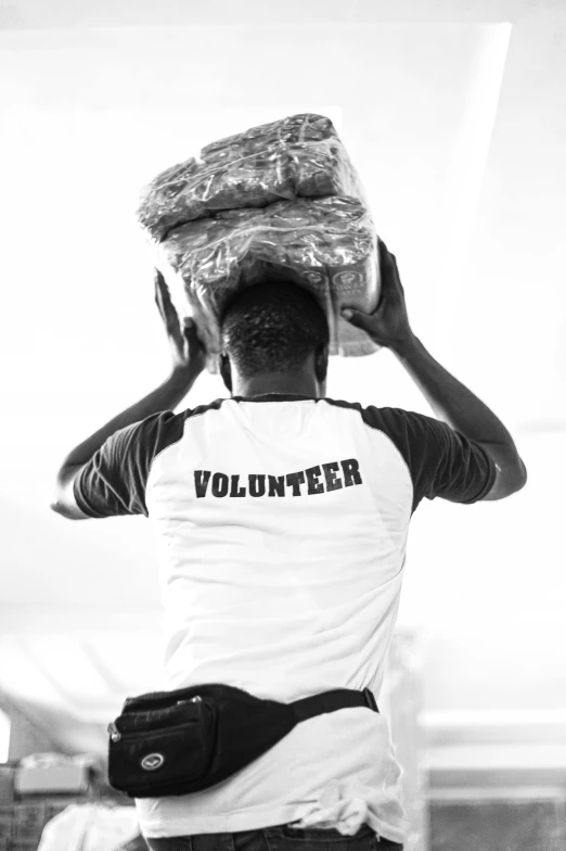 a black and white photo of a man carrying a box on his head, an album cover, pexels contest winner, arte povera, somalia, man in white t - shirt, healthcare worker, back