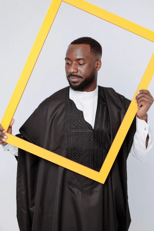 a man holding a picture frame in front of his face, an album cover, inspired by Ras Akyem, pexels contest winner, happening, wearing a grey robe, mkbhd, a handsome man，black short hair, dressed thobe