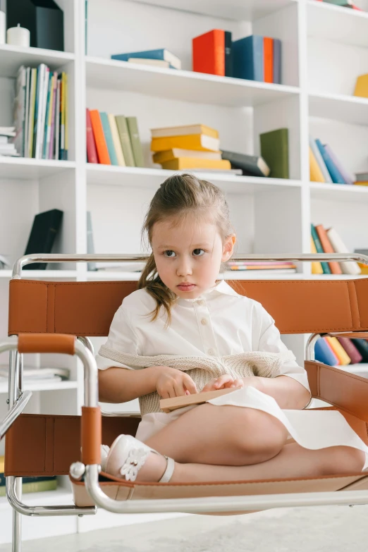 a little girl sitting on a chair in front of a bookshelf, inspired by Elsa Beskow, pexels contest winner, modernism, with serious face expression, sitting in the classroom, gif, architect