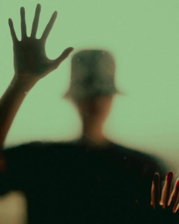 a person standing in front of a window with their hands in the air, a hologram, trending on unsplash, expressionism, hand holding cap brim, faces covered in shadows, translucent and slimy flesh, lgbtq