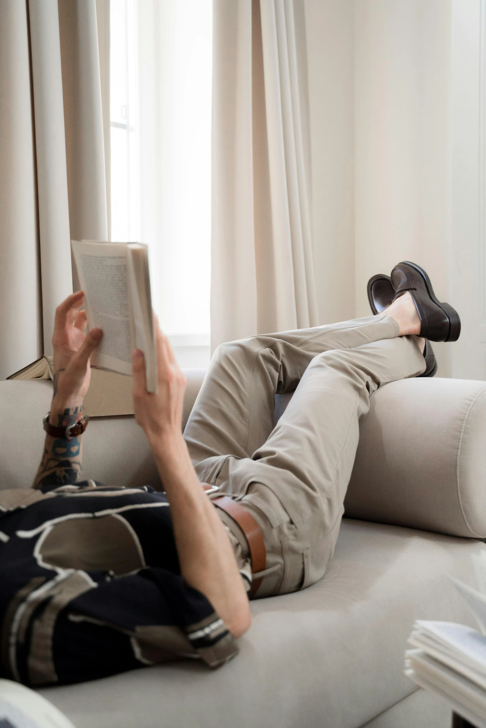 a man laying on a couch reading a book, by Nina Hamnett, trending on reddit, wearing pants, premium quality, mid shot photo