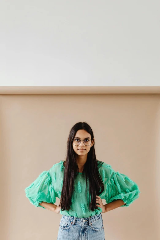 a woman standing with her hands on her hips, by Olivia Peguero, wavy long black hair and glasses, wearing only a green robe, julia hetta, standing in corner of room