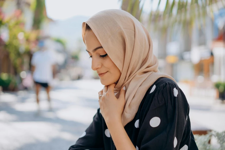 a woman in a hijab looking at her cell phone, trending on pexels, hurufiyya, head turned to the side, polka dot, beige, bosnian