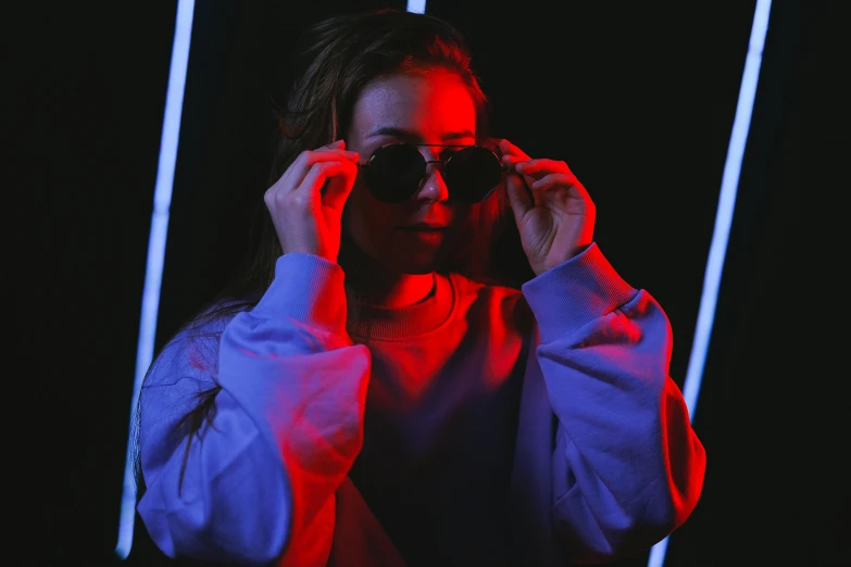 a woman holding a pair of sunglasses in front of her face, inspired by Elsa Bleda, pexels contest winner, red and blue neon, light clothing, portrait soft low light, instagram post