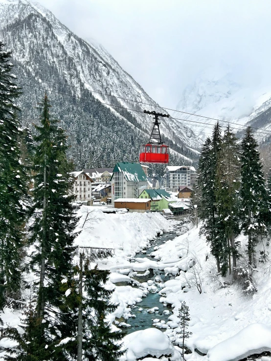 a ski lift going up the side of a mountain, village in the background, photo of green river, with snow covered colourful red, dasha taran