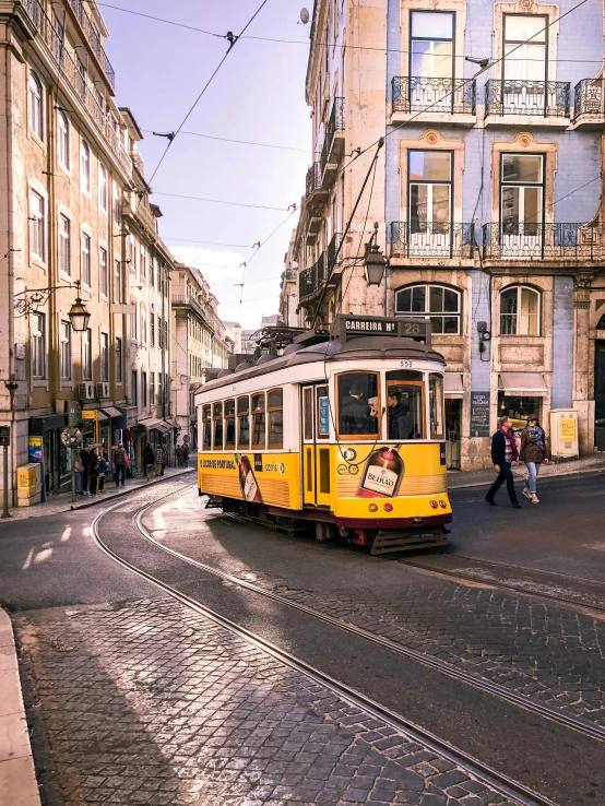 a yellow trolley traveling down a street next to tall buildings, inspired by Almada Negreiros, pexels contest winner, baroque winding cobbled streets, square, slide show, trams