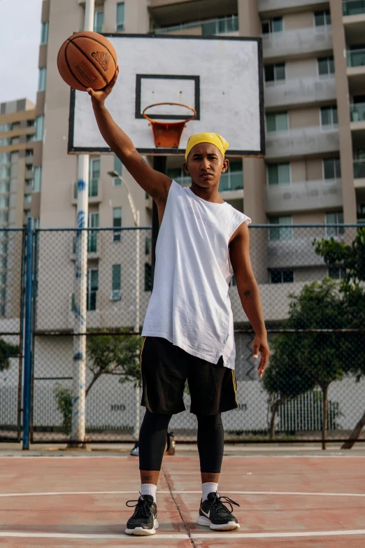 a man standing on top of a basketball court holding a basketball, pexels contest winner, in sao paulo, with rap cap on head, wearing a vest top, ( ( theatrical ) )