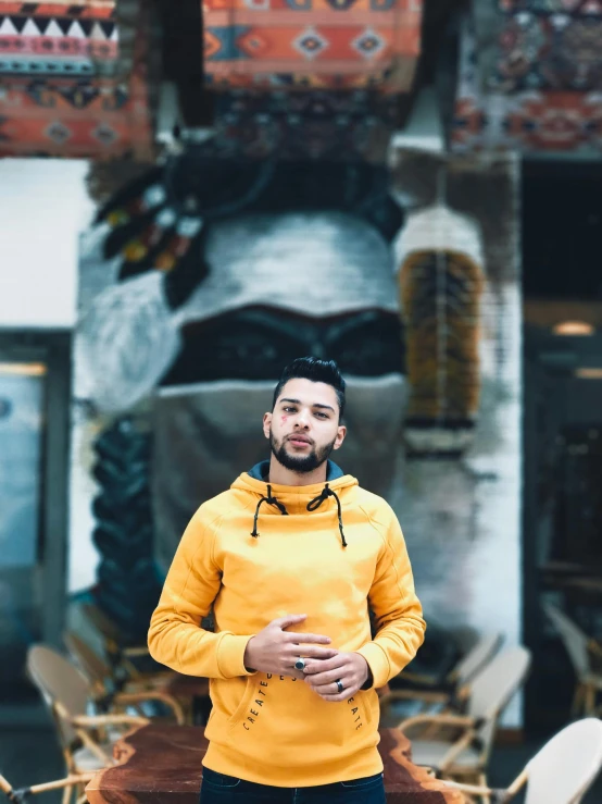 a man in a yellow hoodie standing in front of a building, style of ade santora, avatar image, standing in a restaurant, portrait featured on unsplash