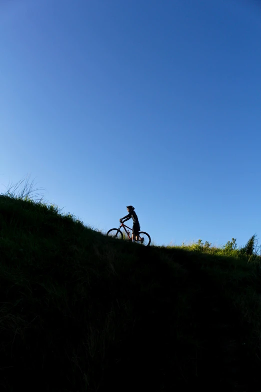 a person riding a bike on top of a hill, te pae, summer evening, clear blue sky, explore