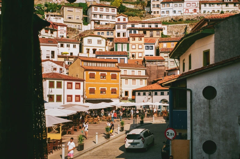 a group of people walking down a street next to tall buildings, a picture, renaissance, cliffside town, bosnian, unsplash photography, square