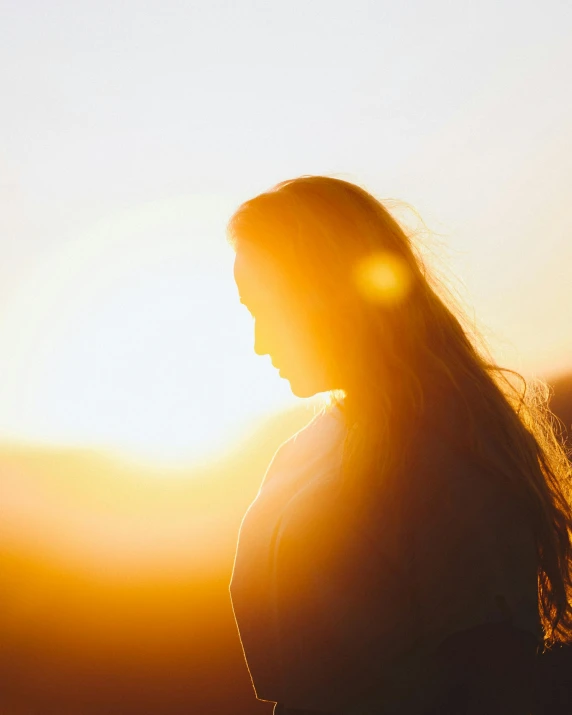 a woman standing in front of the sun, by Christen Dalsgaard, trending on unsplash, light and space, glowing flowing hair, fading rainbow light, looking sad, silhouette :7