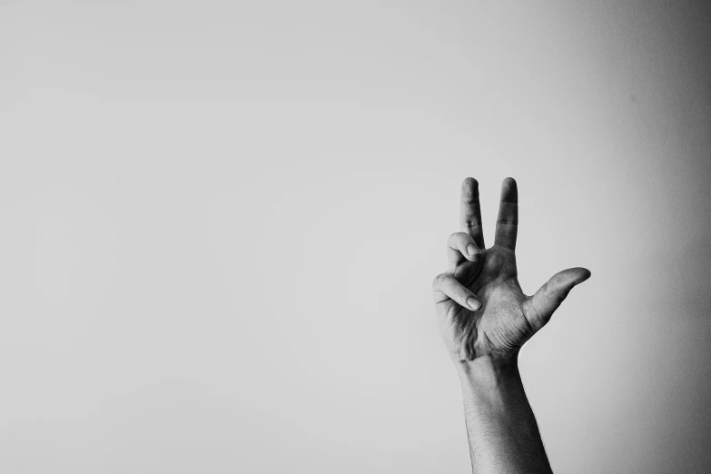a person holding their hand up in the air, a black and white photo, pexels, minimalism, peace sign, background image, rule of three, serpentine pose gesture