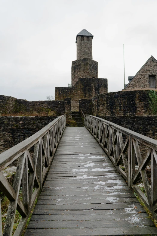 a wooden bridge with a tower in the background, inspired by Limbourg brothers, unsplash, romanesque, deteriorated, overcast, fortress, ground - level view