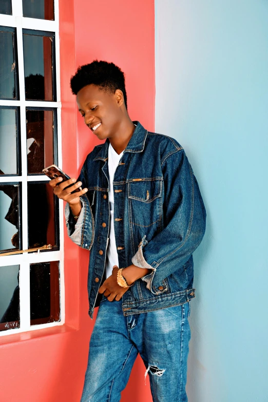 a man standing in front of a window looking at his cell phone, an album cover, by Everett Warner, trending on pexels, wearing a jeans jackets, black teenage boy, smiling, maria borges