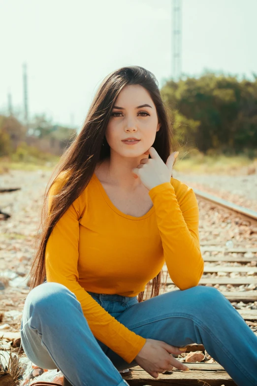 a beautiful young woman sitting on a train track, by Robbie Trevino, yellow clothes, with long dark hair, half body cropping, plain background