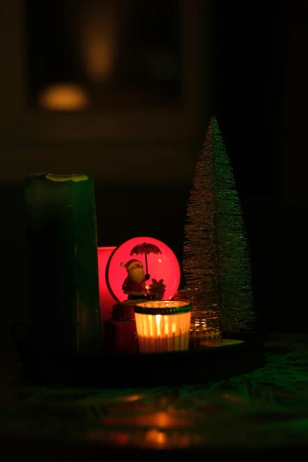 a candle sitting on top of a table next to a christmas tree, green and red radioactive swamp, soft lighing, mini model, with red haze