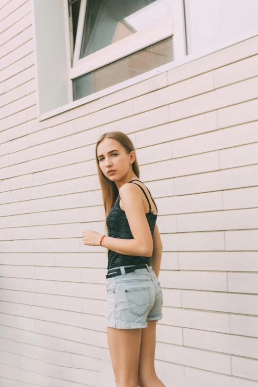 a woman standing in front of a white building, inspired by Elsa Bleda, unsplash, photorealism, tight black tank top and shorts, model エリサヘス s from acquamodels, young teen, gif