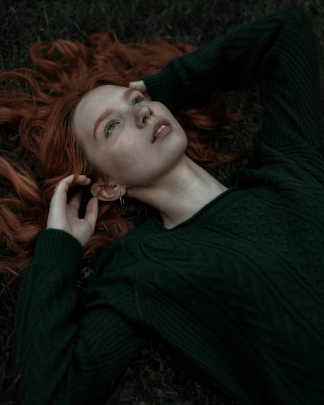 a woman with red hair laying on the ground, inspired by Elsa Bleda, trending on pexels, wearing a dark sweater, lush green, androgynous, accurate image