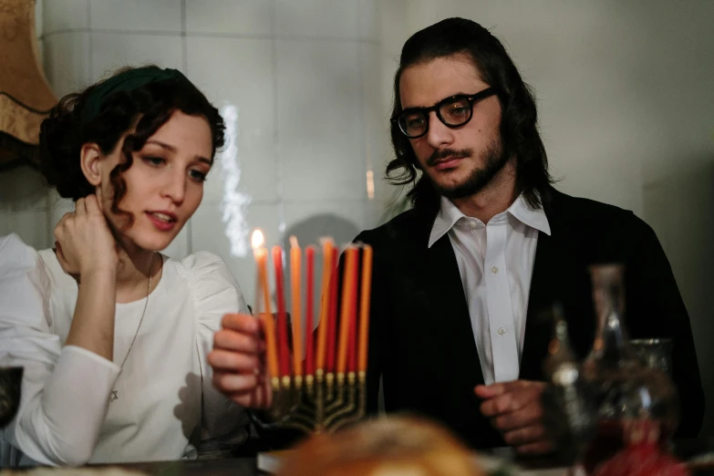 a man and a woman sitting at a table with candles, jewish young man with glasses, 2019 trending photo, square, jen atkin