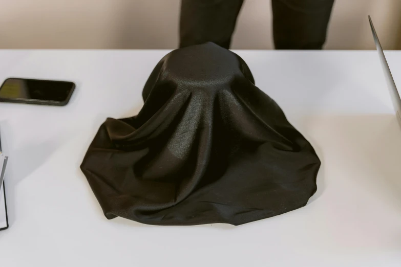 a hat sitting on top of a table next to a laptop, black cloth, shroud, black silky hair, faceless