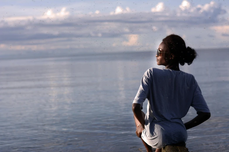 a woman standing on top of a beach next to the ocean, by Pamela Ascherson, unsplash, visual art, jamaica, sitting in front of a lake, photo of a black woman, gazing off into the horizon
