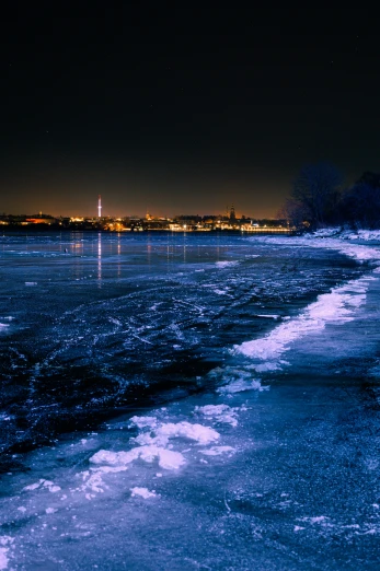 a beach covered in ice next to a body of water, by Antoni Brodowski, night city in the background, hamar, today\'s featured photograph 4k, a mystic river