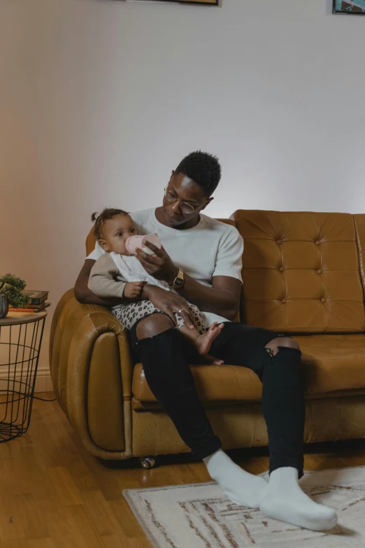 a man sitting on a couch holding a baby, pexels contest winner, essence, 2 1 savage, having a snack, healthcare