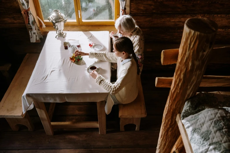 a couple of people that are sitting at a table, by Adam Marczyński, pexels contest winner, arts and crafts movement, inside of a cabin, air shot, white, hansel and gretel