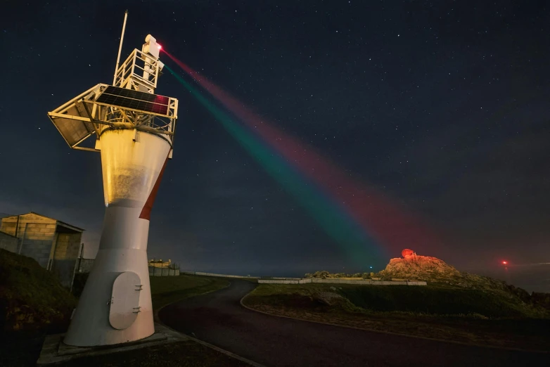 a lighthouse sitting on top of a hill under a night sky, a hologram, by Breyten Breytenbach, unsplash contest winner, rainbow diffraction, red laser, big telescope in front, photographed for reuters