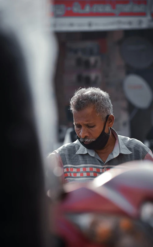 a man wearing a face mask standing next to a motorcycle, pexels contest winner, on an indian street, some grey hair in beard, people shopping, ( ( theatrical ) )