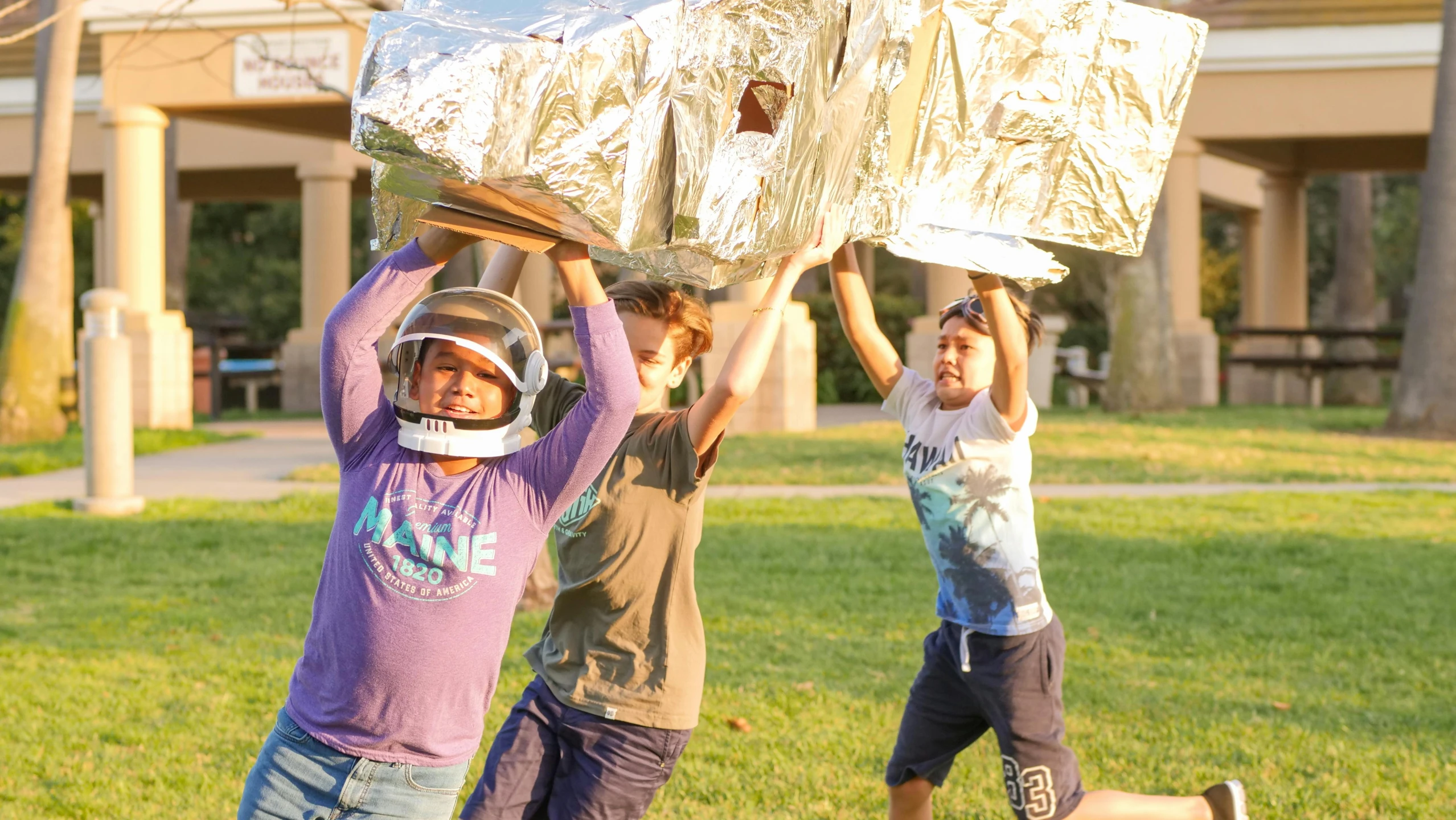 a group of young men standing on top of a lush green field, astronaut helmet, holding up a large shield, kids playing, with the sun shining on it