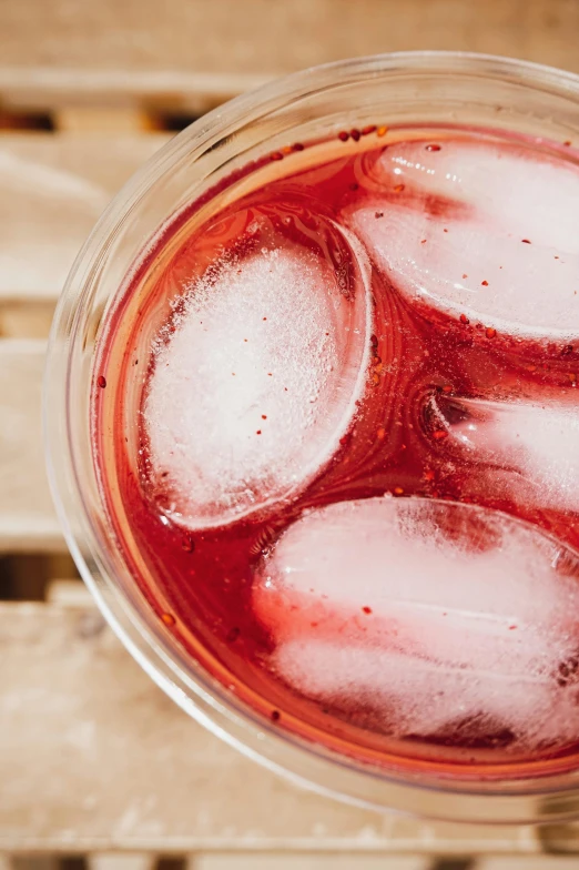 a glass filled with ice sitting on top of a wooden table, inspired by Jacopo Bellini, trending on pexels, renaissance, hibiscus, birdseye view, detailed product image, magenta