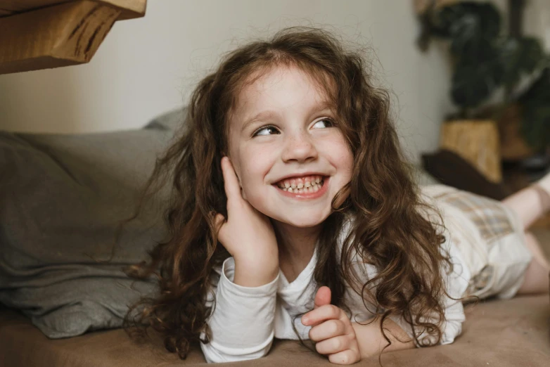 a little girl laying on top of a bed, pexels contest winner, happening, big teeth, woman with braided brown hair, looking to the side, close up character