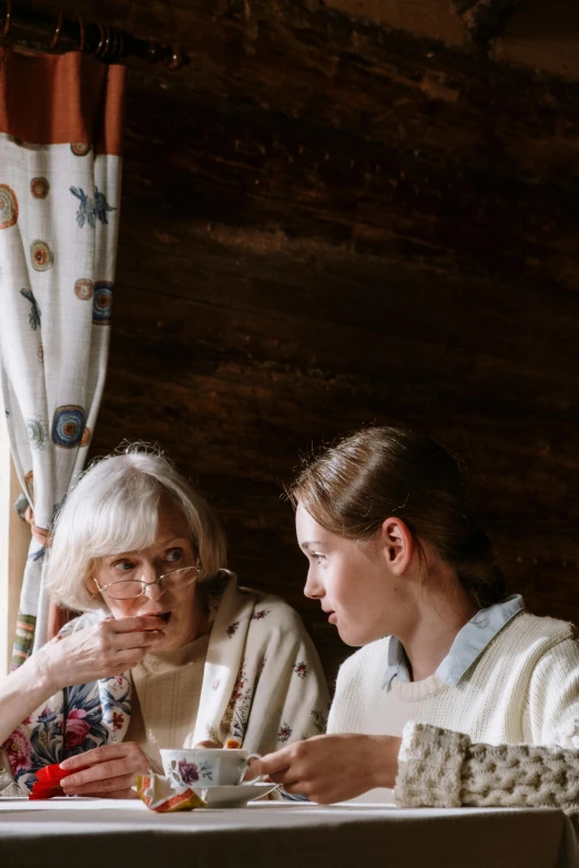 two women sitting at a table eating food, a portrait, by Adam Marczyński, trending on pexels, renaissance, in a cabin, an elderly, soft light 4 k, teenage girl