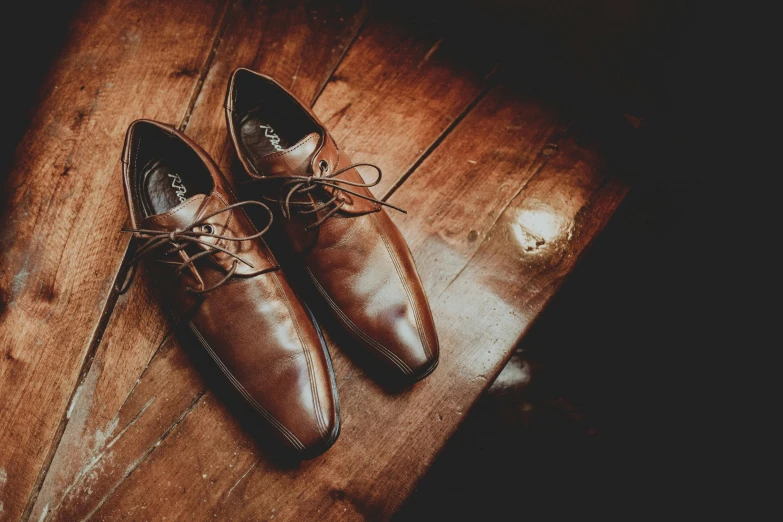 a pair of brown shoes sitting on top of a wooden floor, on a table