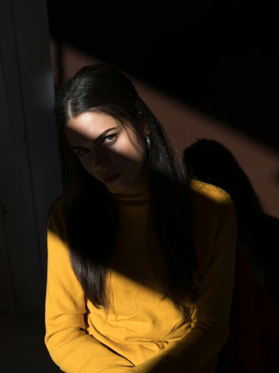 a woman sitting on a chair in a dark room, inspired by Elsa Bleda, unsplash, realism, glowing yellow face, alexandria ocasio cortez, portrait casting long shadows, teenage girl