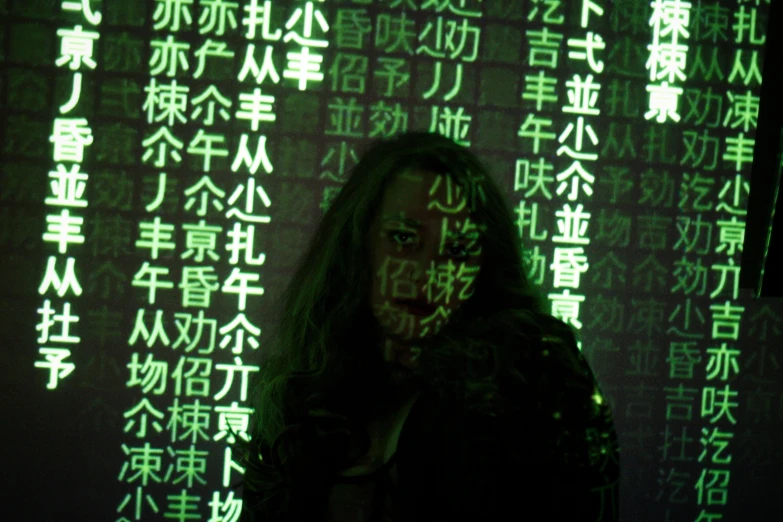 a person standing in front of a wall with asian writing on it, ascii art, dramatic green lighting, chinese woman, behind the scenes photo, covered in runes