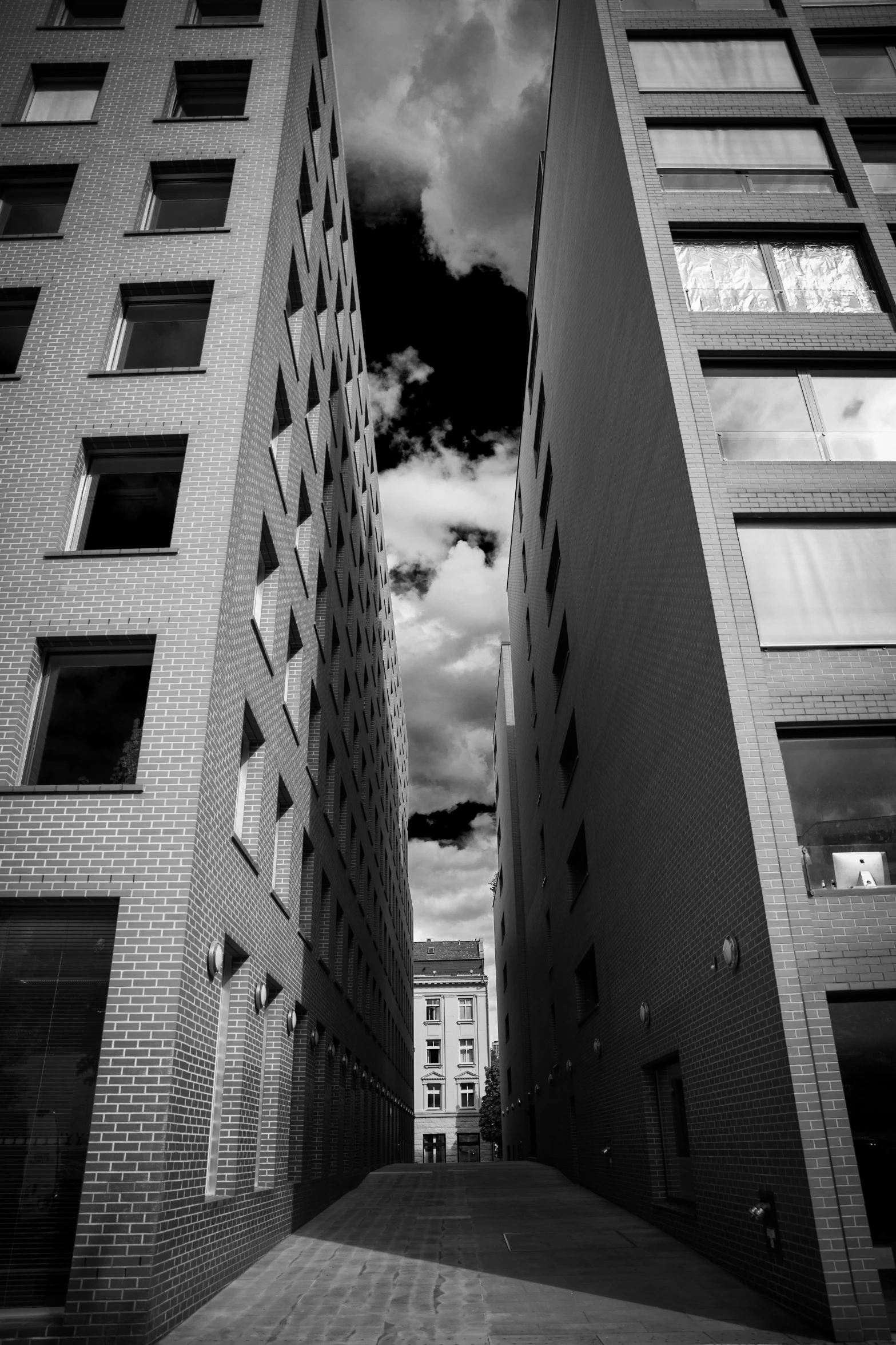 a black and white photo of two tall buildings, inspired by André Kertész, unsplash, impending doom in an alleyway, fancy clouds, swedish urban landscape, burning buildings