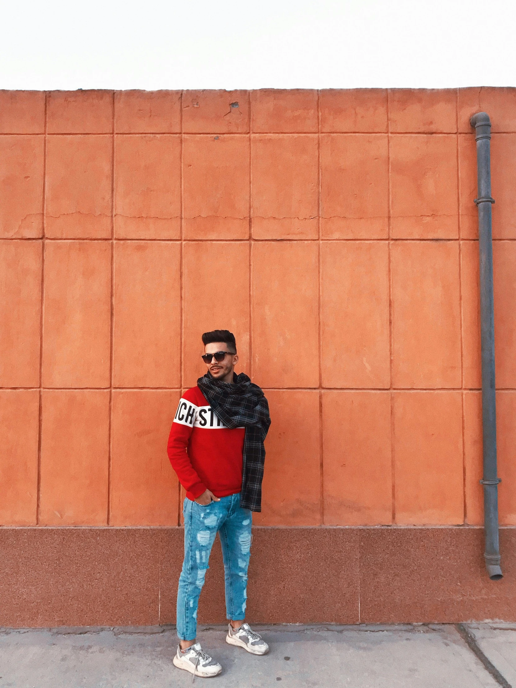 a man standing in front of a brick wall, by Julia Pishtar, pexels contest winner, cool red jacket, riyahd cassiem, full body pose, ( ( dark skin ) )