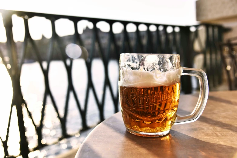a glass of beer sitting on top of a wooden table, on a bridge