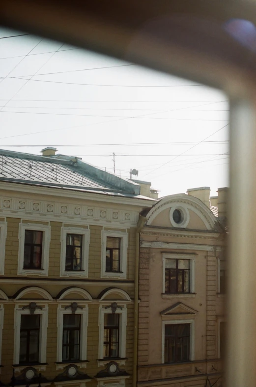 a view of a building through a window, inspired by Mikhail Yuryevich Lermontov, rounded roof, far away from camera, hiding in the rooftops, neoclassical style