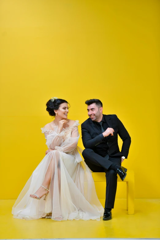 a man in a tuxedo sitting next to a woman in a dress, a portrait, inspired by Nadim Karam, pexels contest winner, yellow backdrop, bride and groom, square, slide show