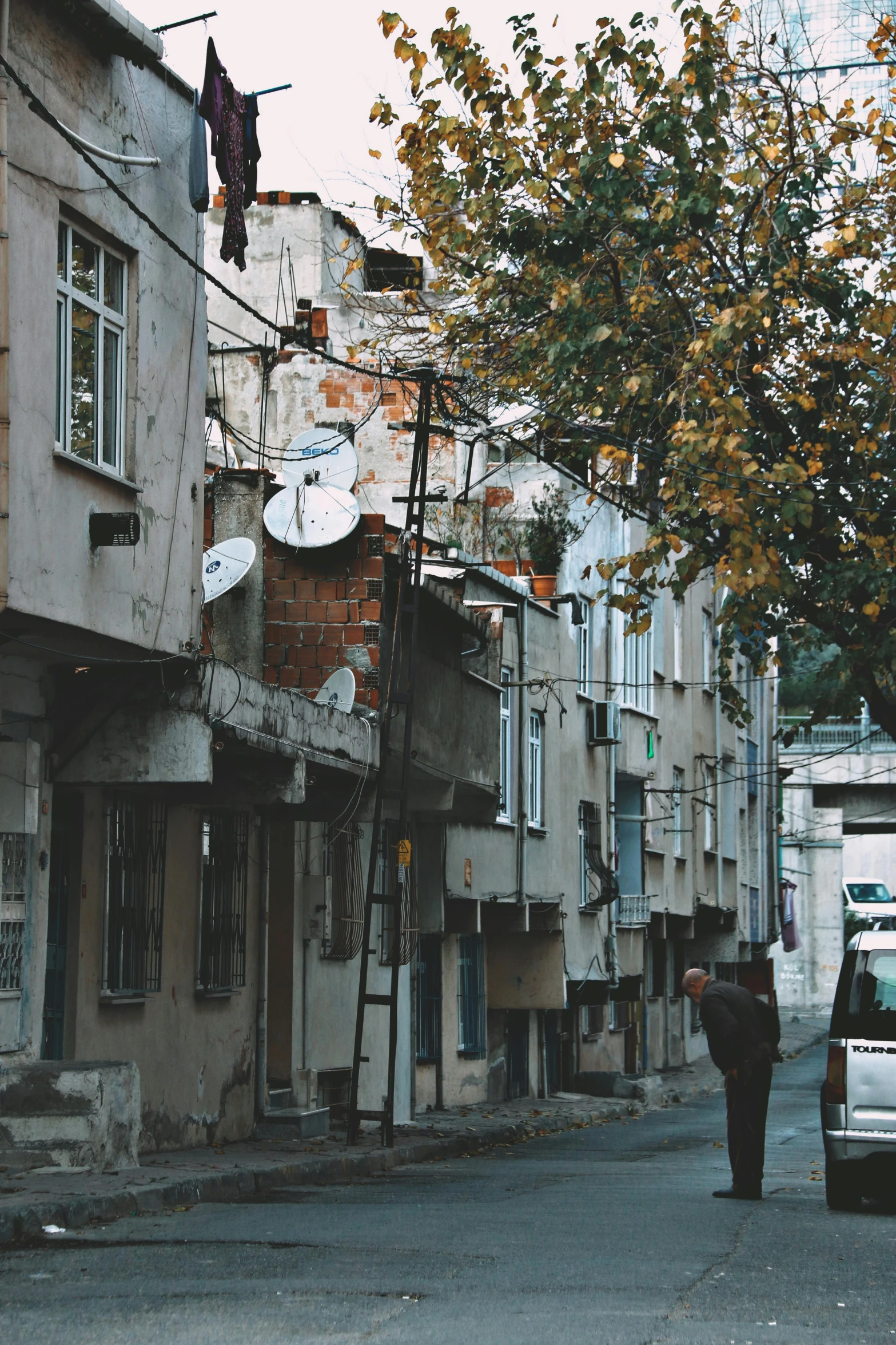 a white van driving down a street next to tall buildings, an album cover, by Lucia Peka, pexels contest winner, renaissance, old ruins, turkish and russian, satellite dishes, late autumn