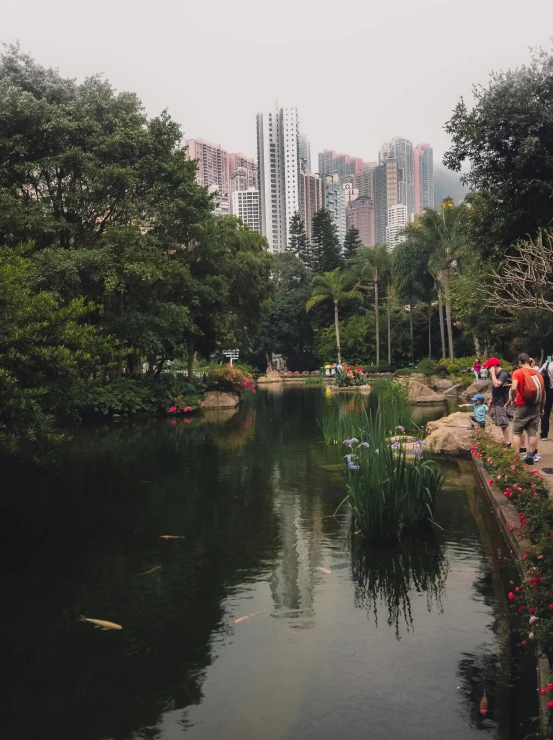 a group of people standing next to a body of water, by Patrick Ching, forest setting with skyscrapers, gardening, low quality photo, high quality image