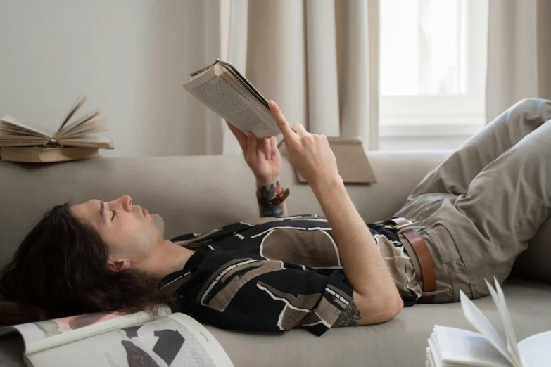 a woman laying on a couch reading a book, inspired by Gillis Rombouts, trending on pexels, handsome man, joe keery, casually dressed, hozier