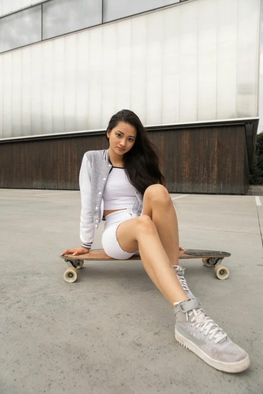 a woman sitting on a skateboard in front of a building, white outfit, cindy avelino, grey skin, fit girl